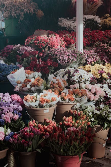An outdoor floral display at Romford Market showcasing a vibrant assortment of fresh flowers arranged in various containers and buckets. The display includes an abundance of chrysanthemums, carnations